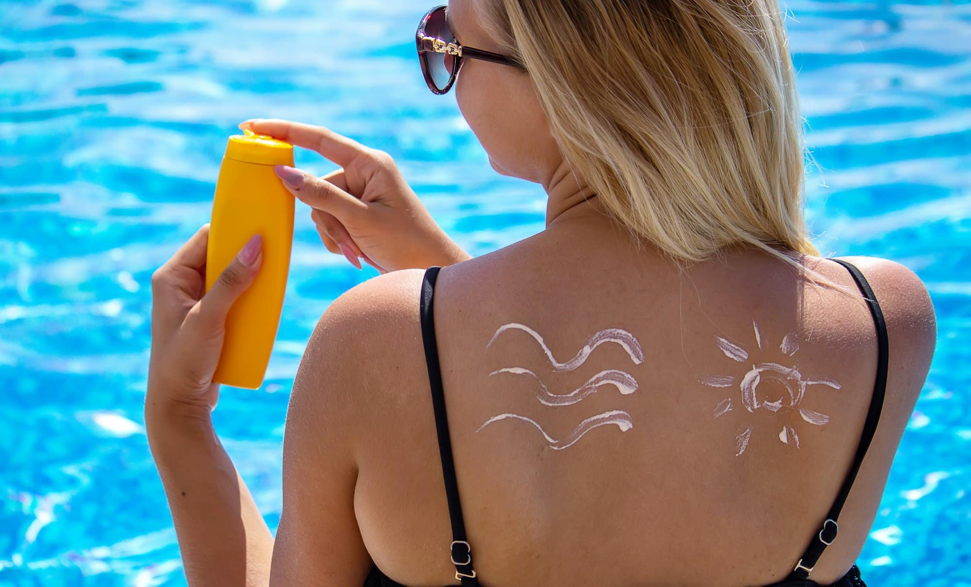 Girl with a drawing of the sun on her back with sun cream. Relaxation by the pool.