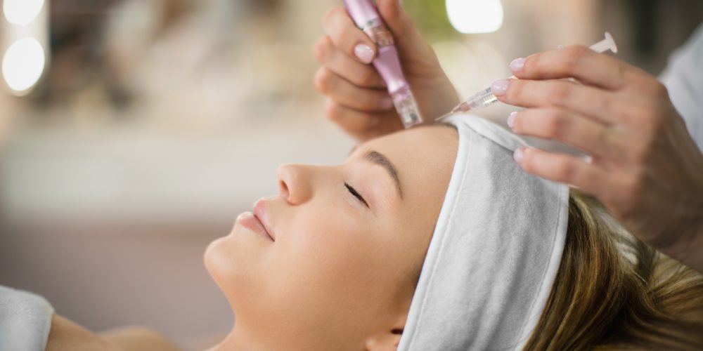 Unrecognizable beautician performs facial treatment on a young woman at beauty salon.