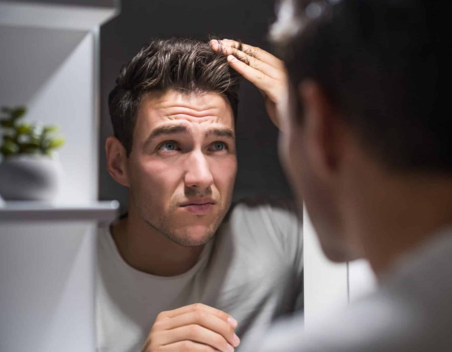 Worried man is looking his hair in the mirror.